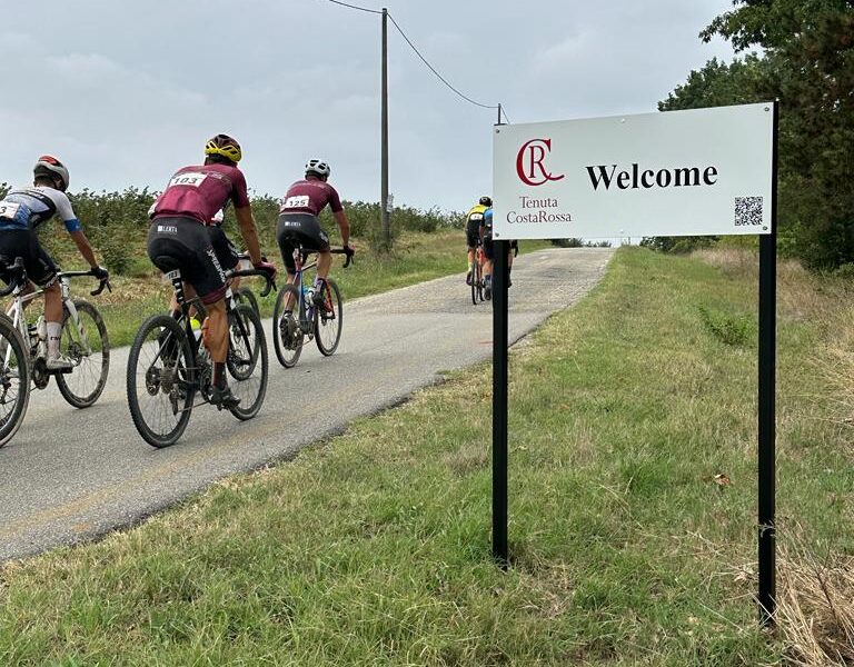 Cyclists passing Tenuta CostaRossa Welcome sign